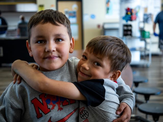 Two boys happily hugging each other in the school cafeteria.