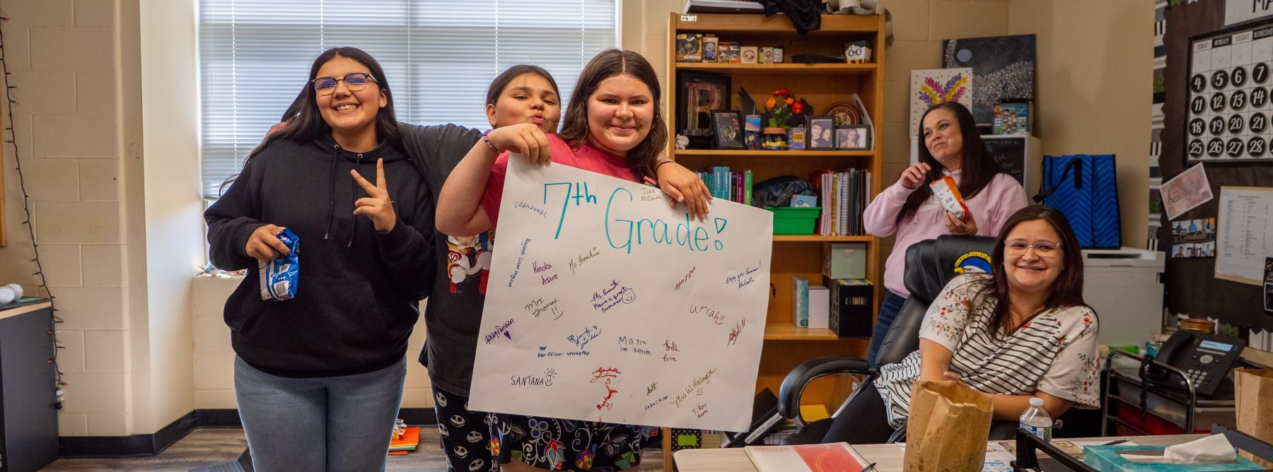 A group of students proudly holds up a sign, smiling and engaging with each other.
