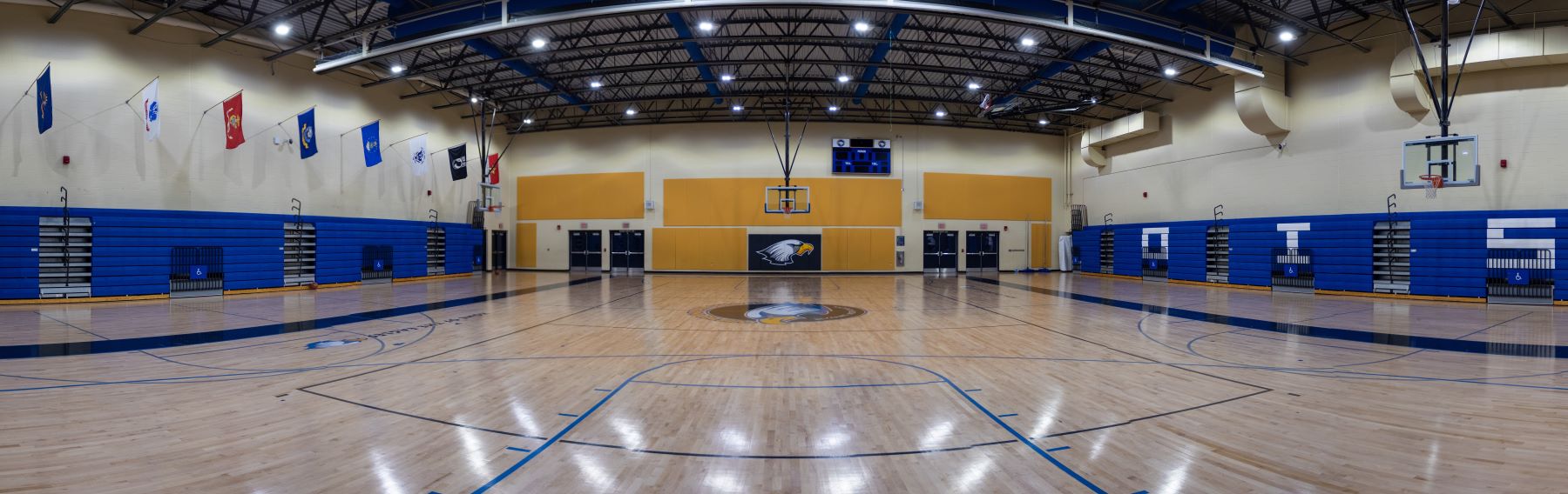A basketball court in the school gym featuring bright blue walls and vibrant yellow floors, ready for a game.