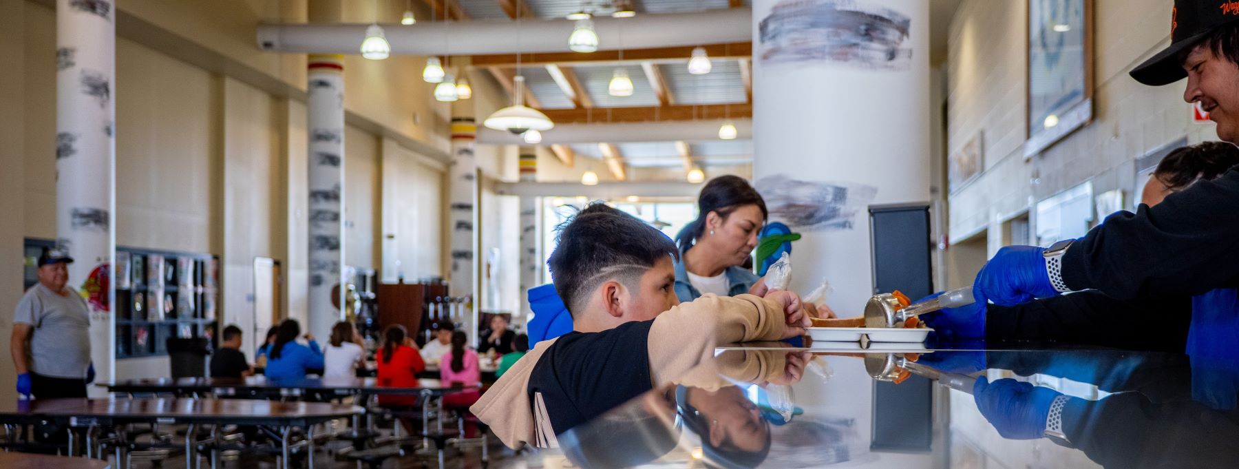 A student receives food in a bustling school cafeteria environment.