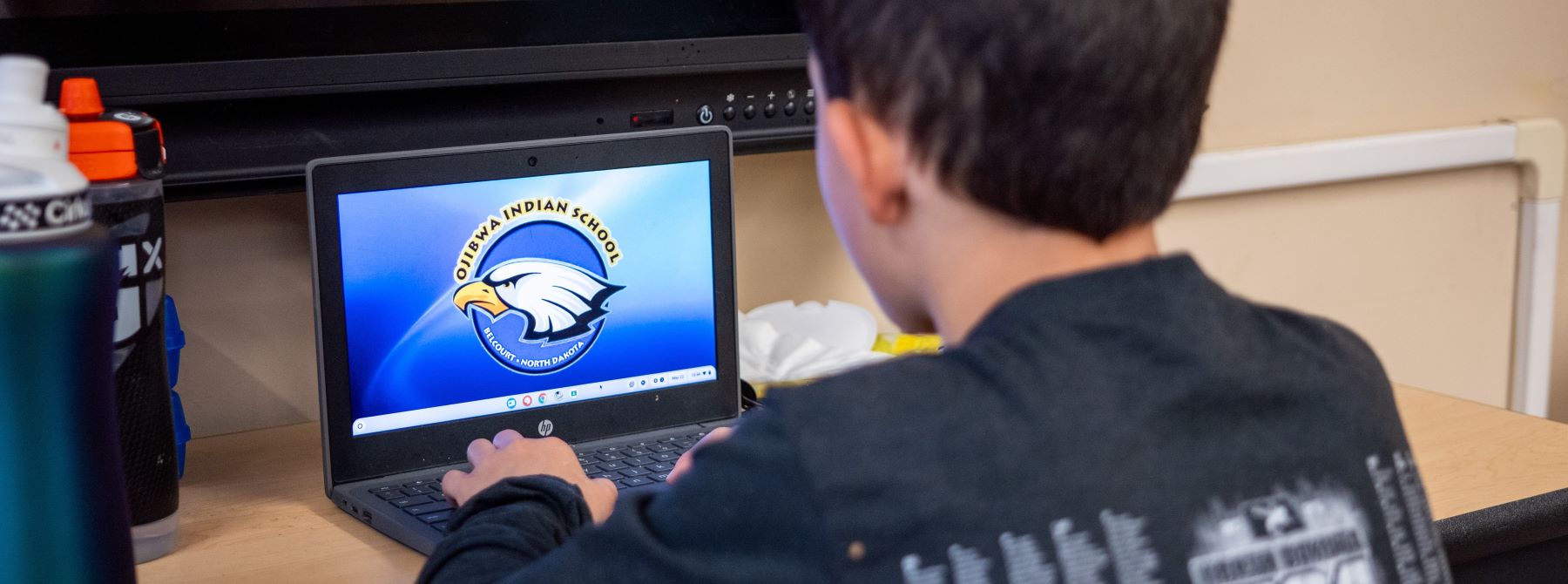 A student focused on a laptop featuring school logo, engaged in his work or study.