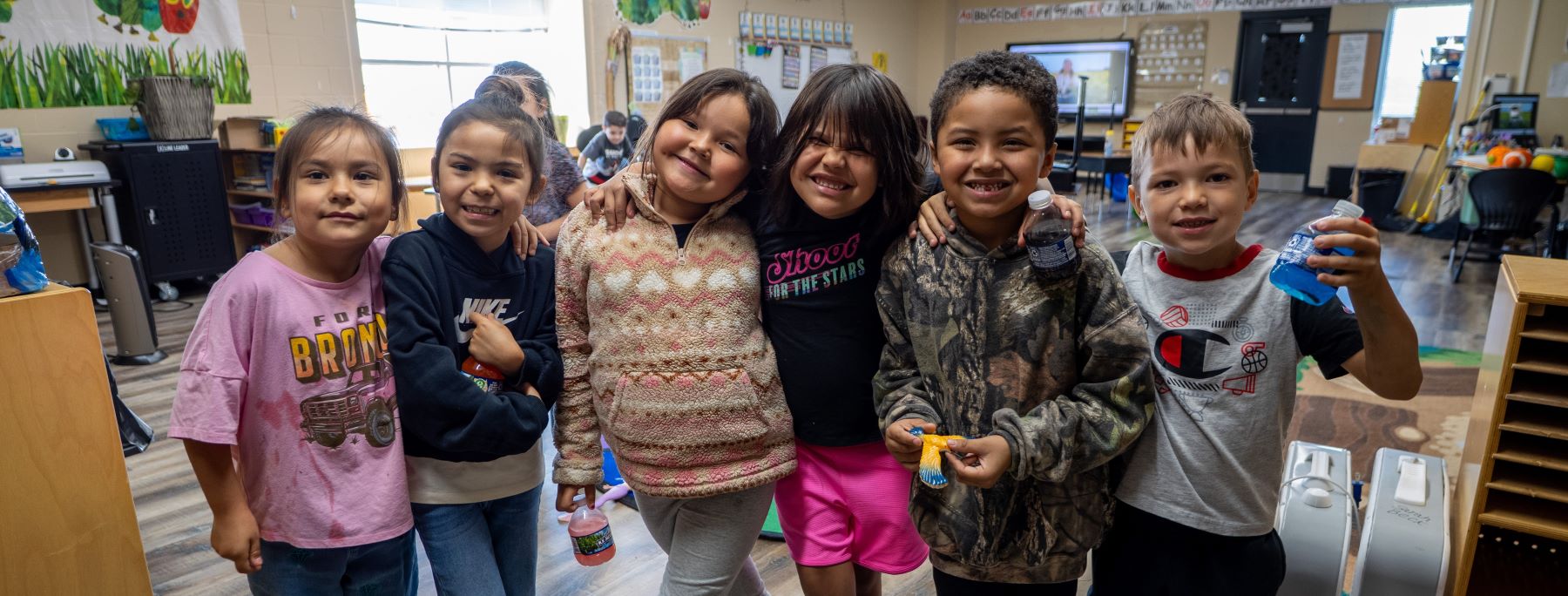 A group of smiling students poses together for a photo in their colorful classroom.