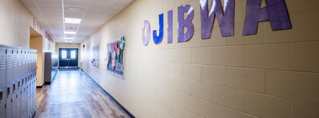 A school hallway lined with lockers, featuring a sign that reads "Ojibwa" prominently displayed on the wall.